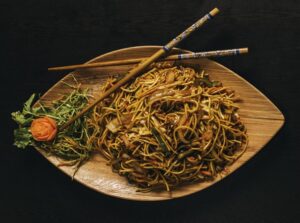 A noodle dish on a wooden plate with chopsticks